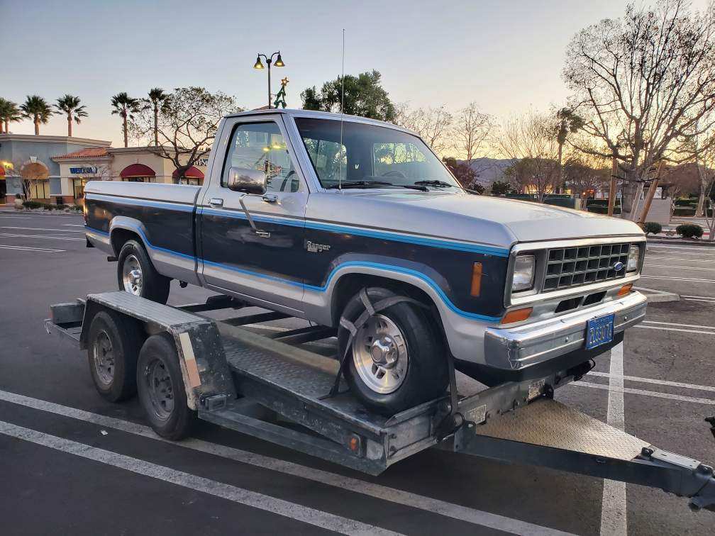 Classic blue pickup truck parked on a trailer in a parking lot.