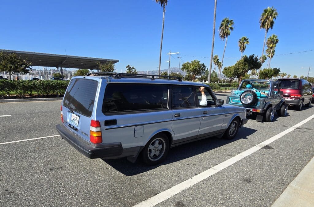 A vintage silver station wagon parked in a sunny lot with palm trees.