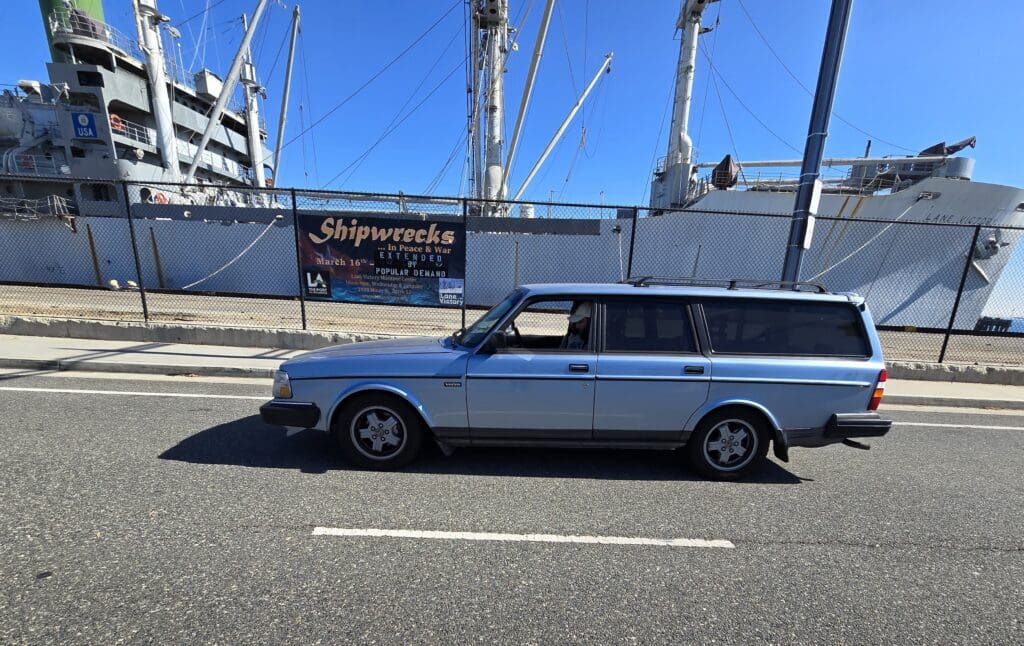 Classic blue Volvo station wagon parked by a docked ship.