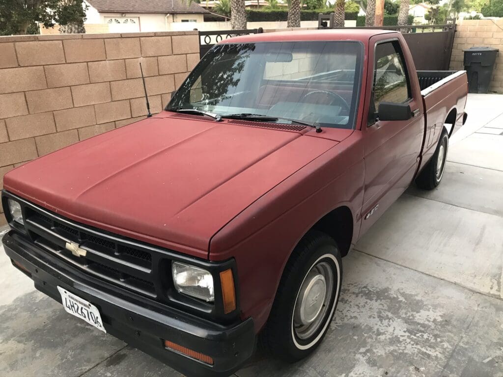 A classic red compact pickup truck parked in a driveway.