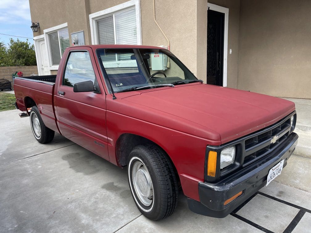 A red vintage pickup truck parked on a driveway near a house.