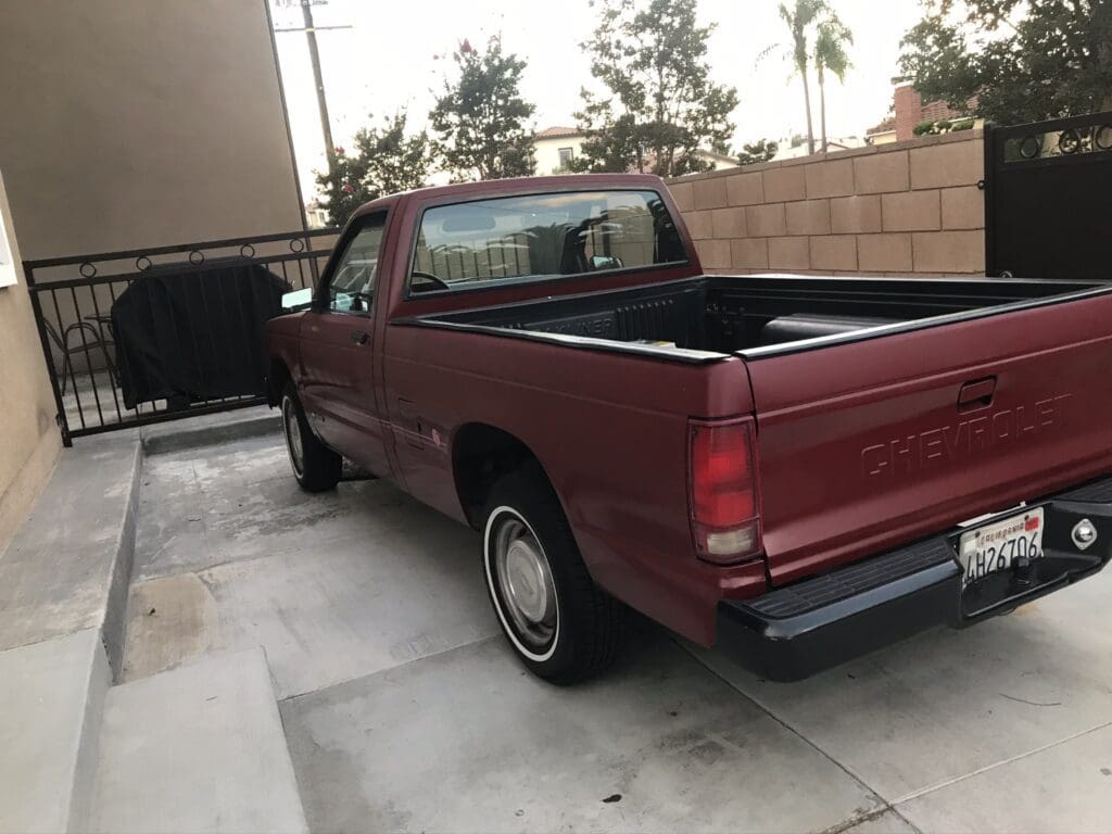 Red pickup truck parked in a driveway beside a brick wall.
