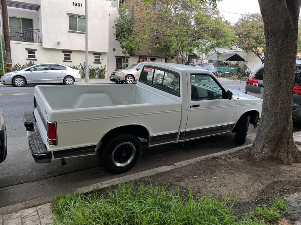 A white pickup truck parked on a residential street with a few cars and apartment buildings.