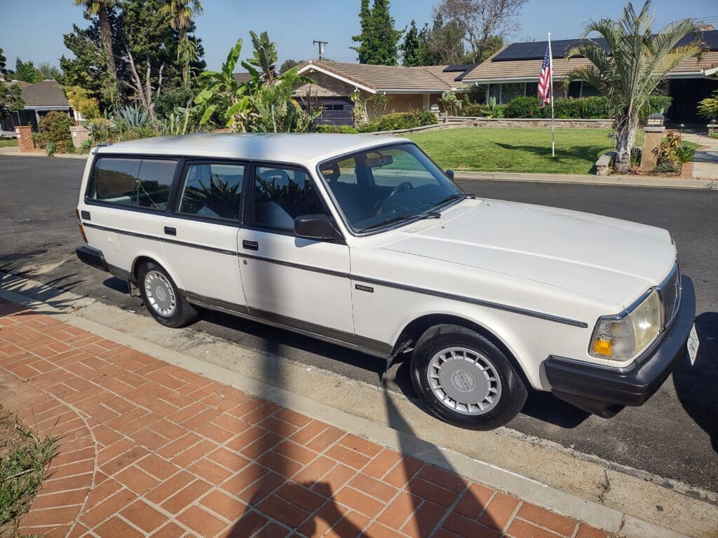 Classic white station wagon parked on a driveway under sunlight.