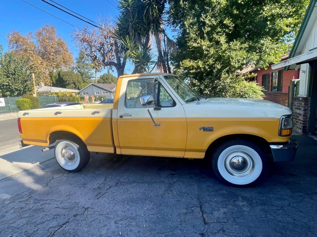 Vintage yellow and white pickup truck parked under trees.