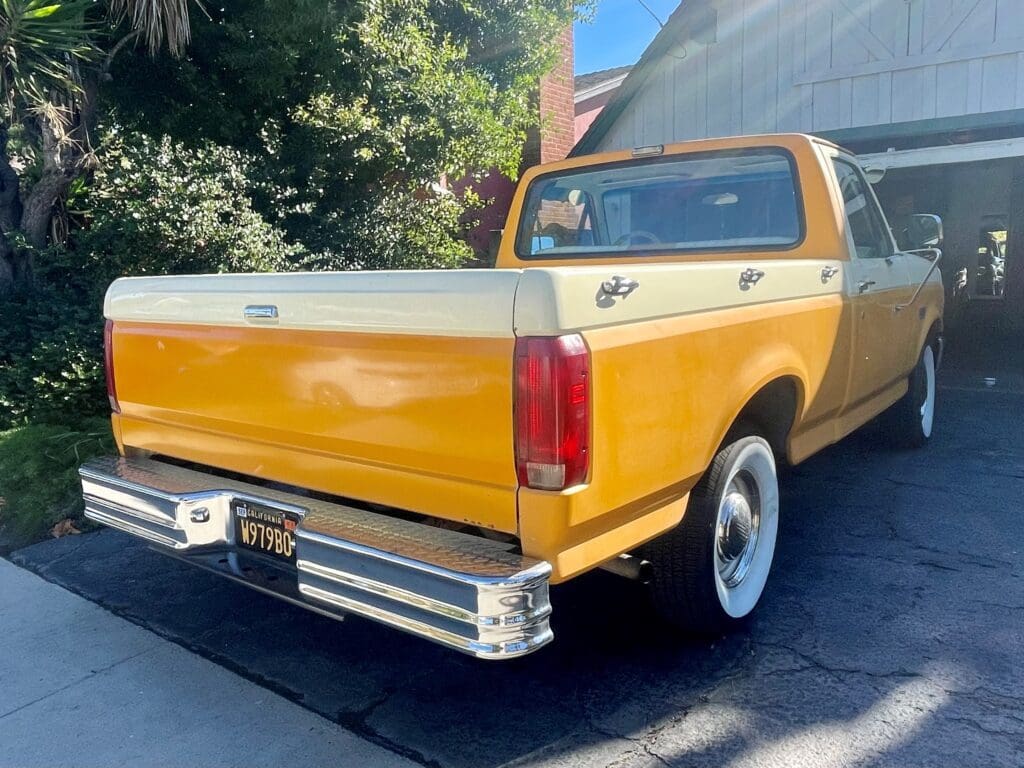 Vintage yellow and white pickup truck parked under trees.