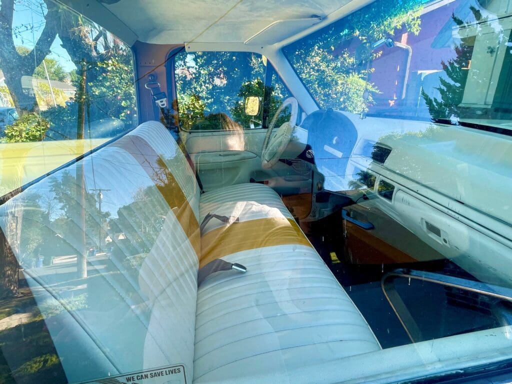 Vintage car interior with white leather seats and visible reflections.