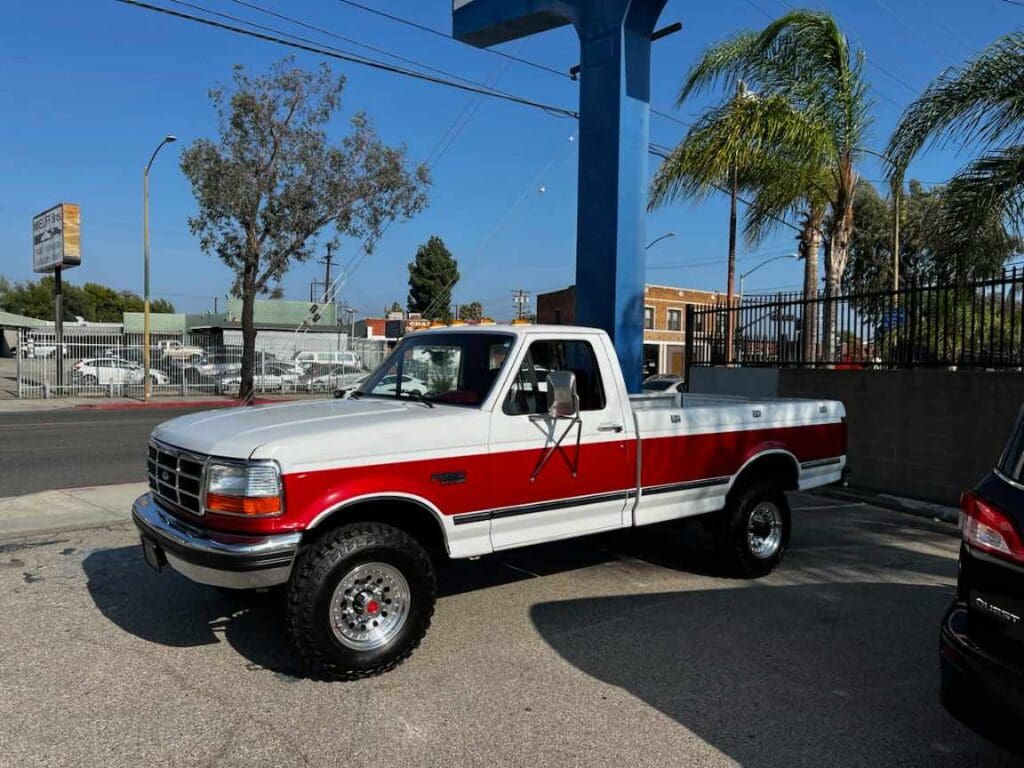 Vintage red and white pickup truck parked outdoors on a sunny day.