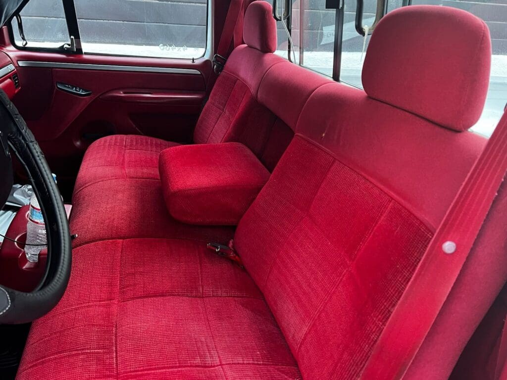 Red fabric seats inside a vehicle with a center armrest.