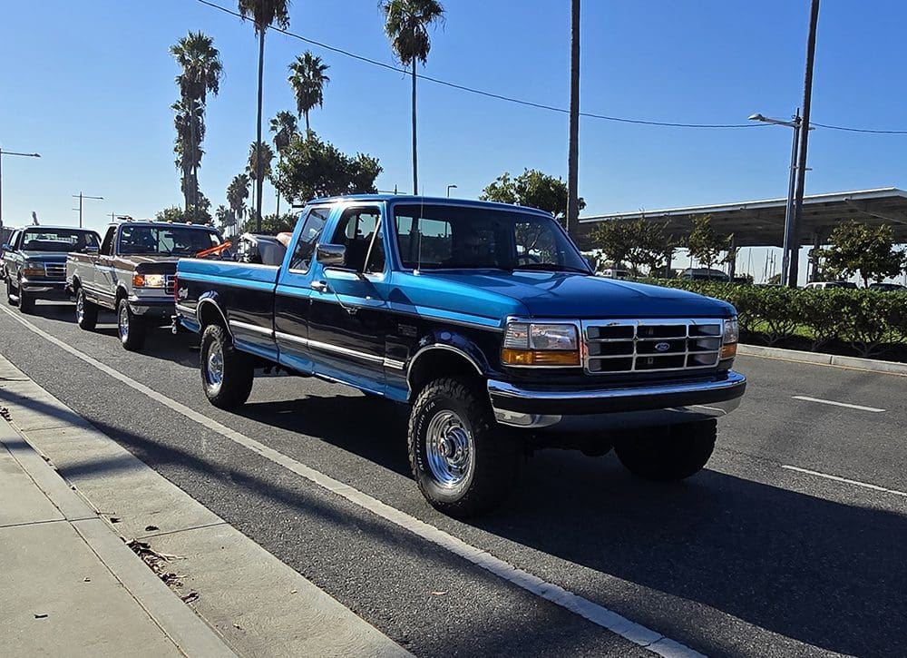 Classic blue pickup truck parked on a sunny street with palm trees.