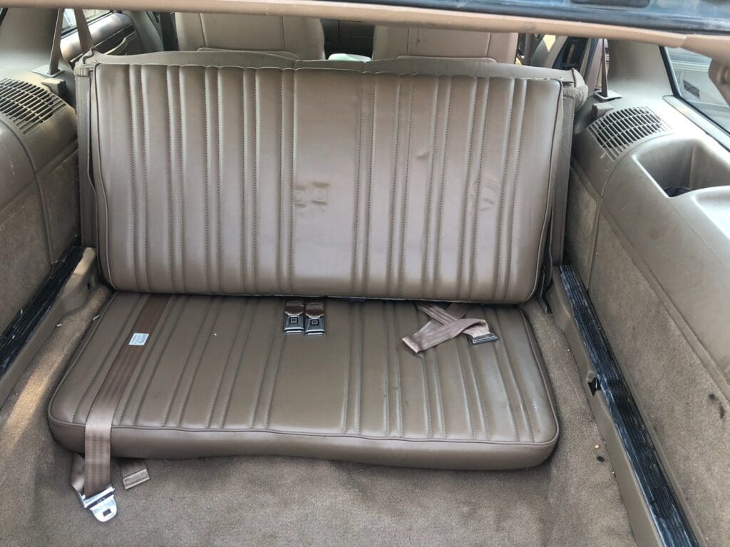 Beige car backseat with seat belts and some small items.
