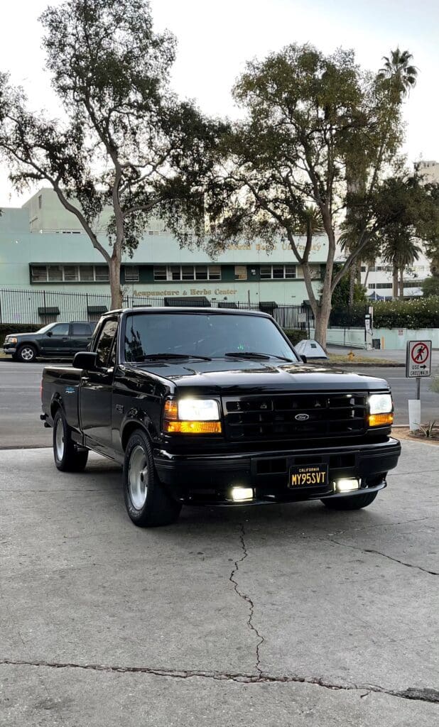 Black pickup truck parked on a street with trees in the background.