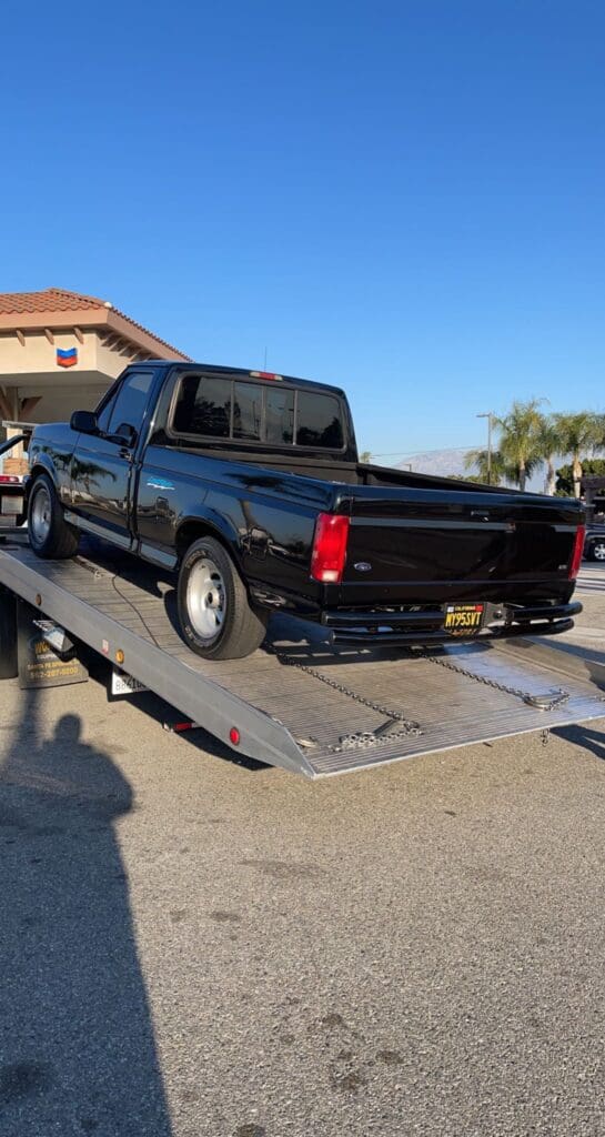 Black pickup truck loaded on a flatbed tow truck on a sunny day.