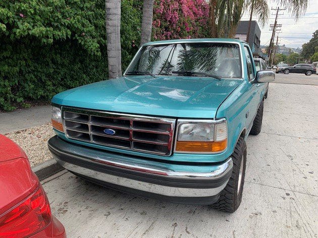 Teal Ford pickup truck parked on a street near greenery.