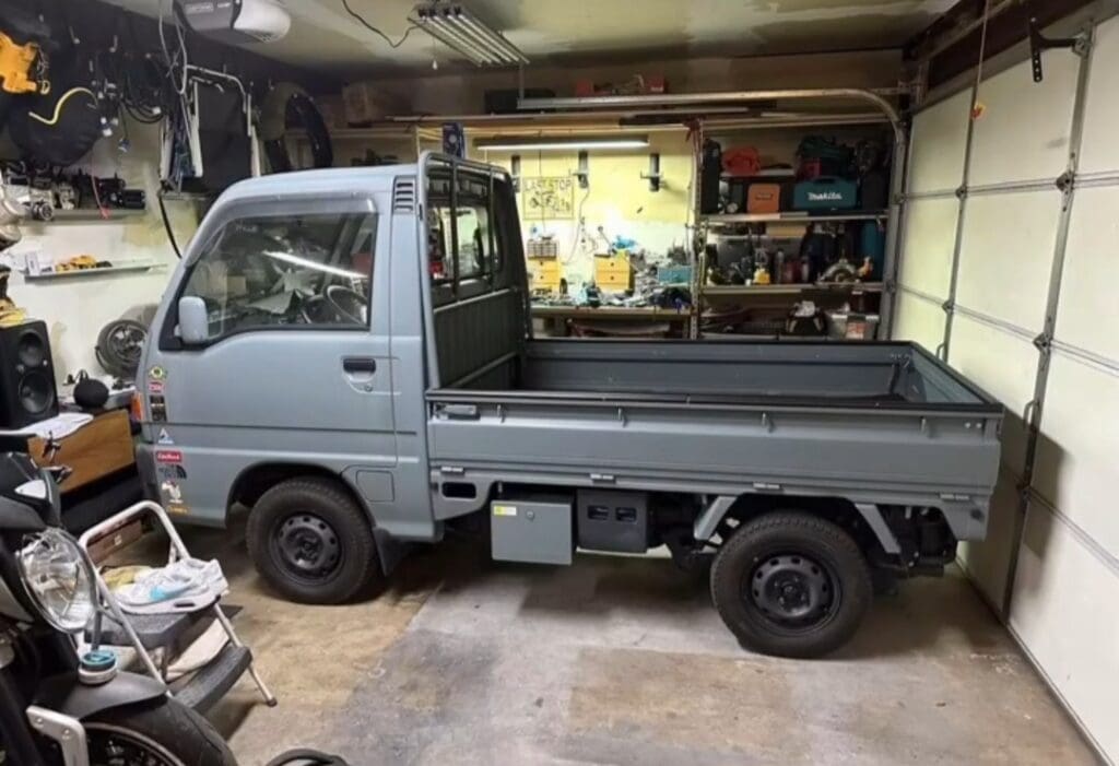 Small gray pickup truck parked inside a garage filled with tools and equipment.