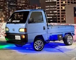 Small blue mini truck with neon underglow parked at night.