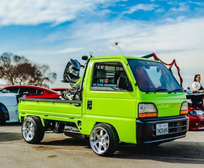 Bright green mini truck carrying a motorcycle under a blue sky.