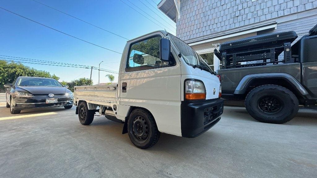 A small white pickup truck parked outdoors next to a building.