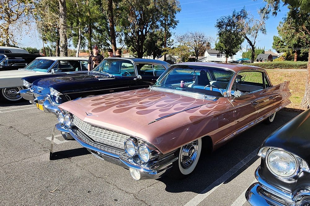 Classic pink Cadillac with flame decals parked outdoors.