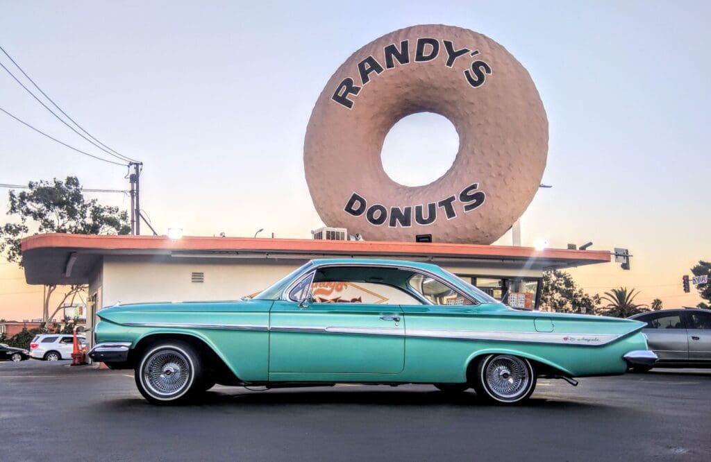 Classic turquoise car parked outside Randy's Donuts with giant donut sign.