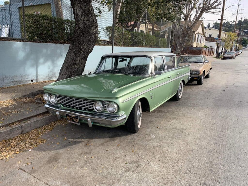 A vintage green station wagon parked on a street beside a tree.