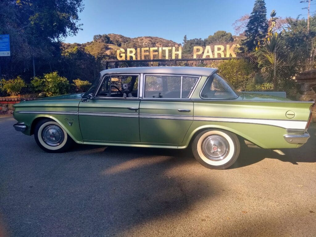 Classic green car parked near Griffith Park sign at sunset.