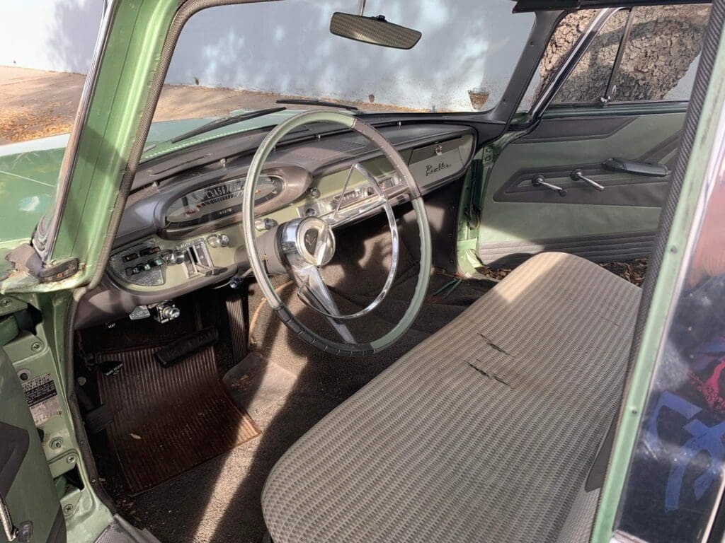 Interior of a vintage green car with a classic steering wheel and bench seat.