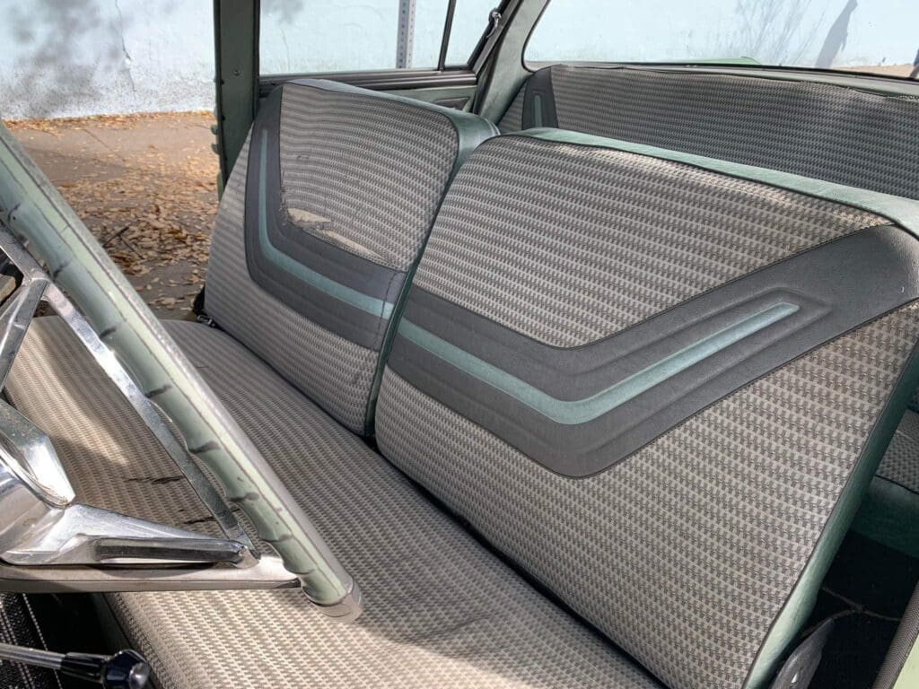 Vintage car interior with patterned bench seat and simple steering wheel.