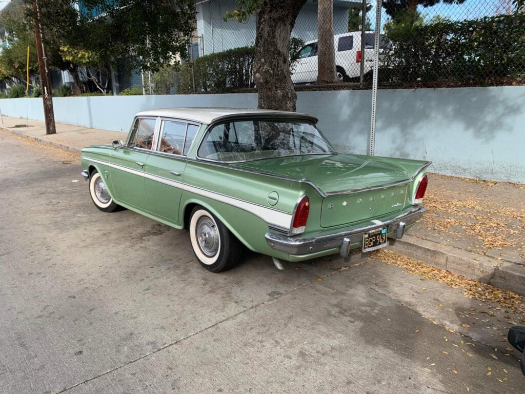 Classic green vintage car parked by the curb under a tree.