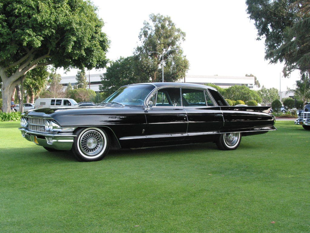 Classic black 1960s luxury car parked on green grass.