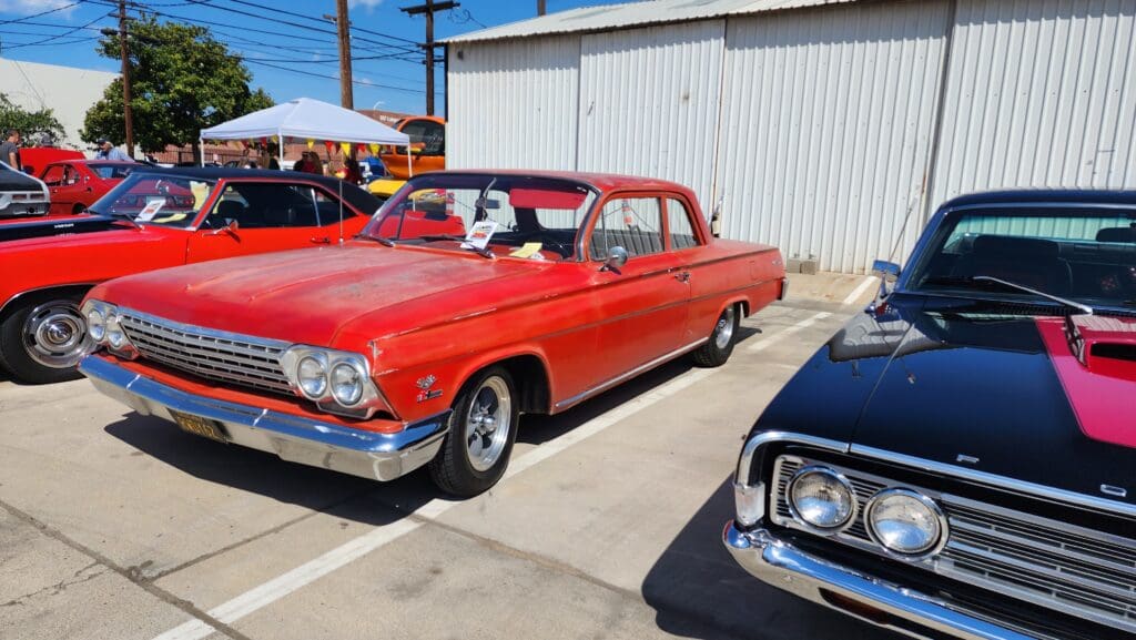 Classic red vintage car parked beside other vehicles at an outdoor event.