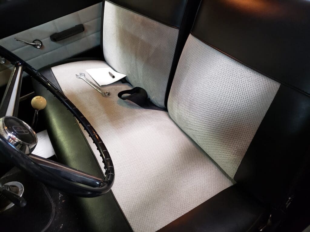 Interior of a car showing clean, white floor mats and black seatbelt.