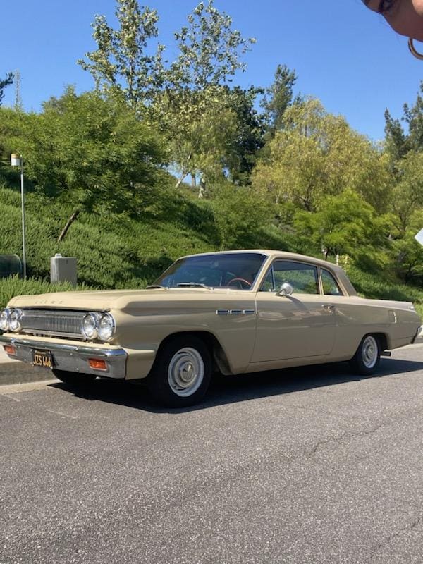 Classic beige 1960s car parked on a sunny street.