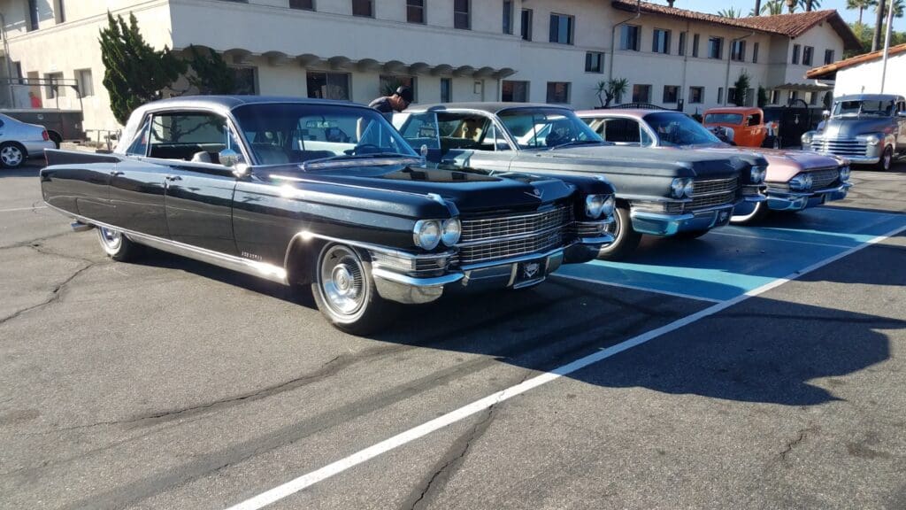 Two classic black vintage cars parked side by side in a sunny lot.
