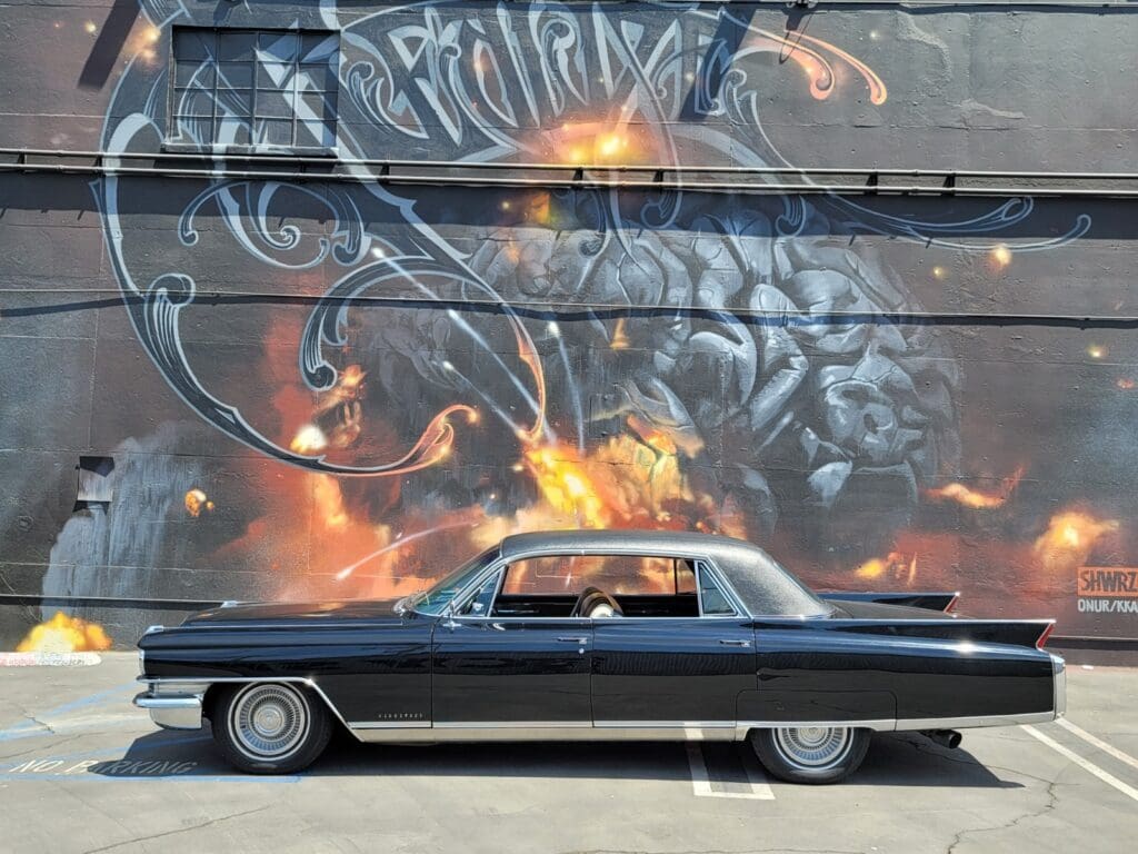 Classic black car parked in front of a fiery mural with a man's face.