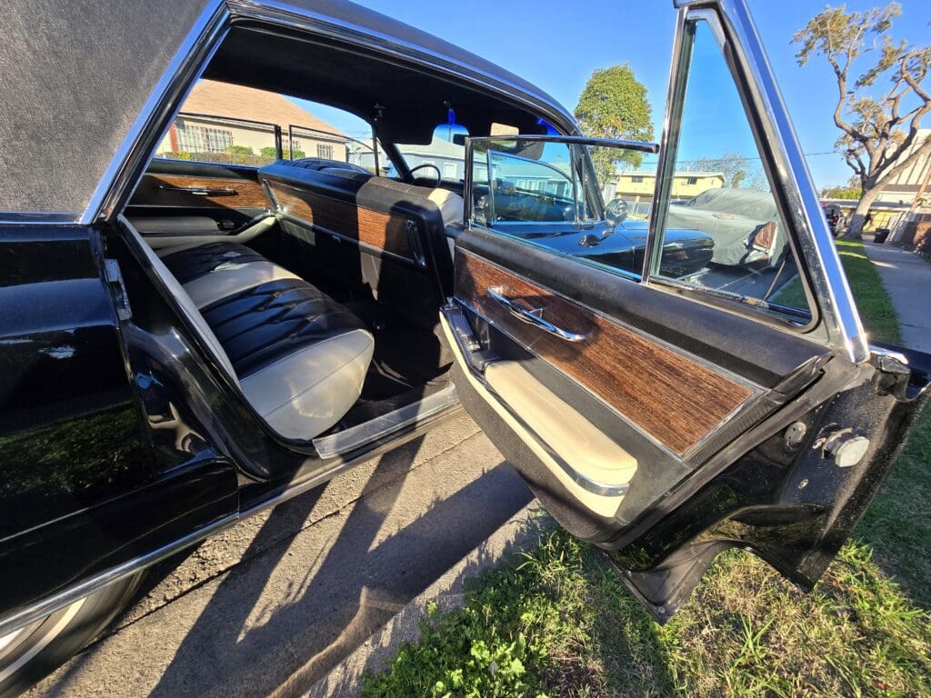 Open car door showing interior of a vintage vehicle with black seats and wooden paneling.