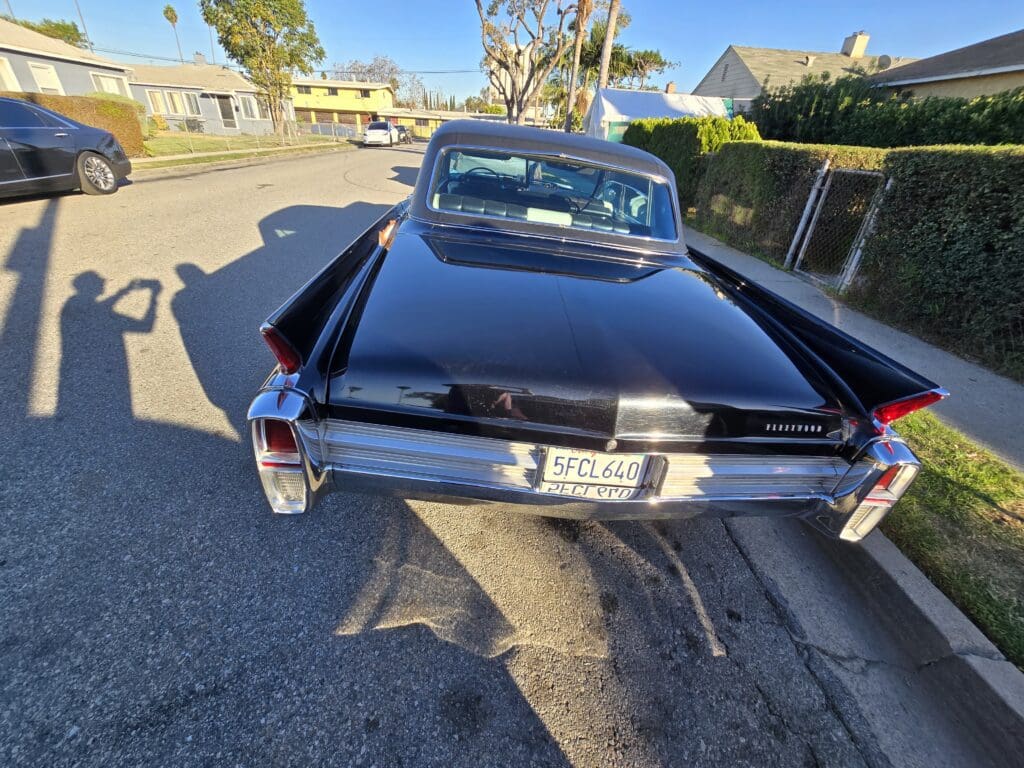 Rear view of a classic black car parked on a sunny street.
