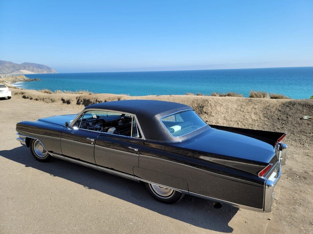 Classic black vintage car parked by a scenic coastal road.