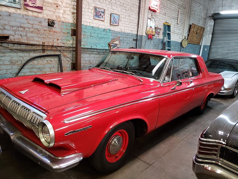 A shiny red vintage car with a hood scoop parked indoors.