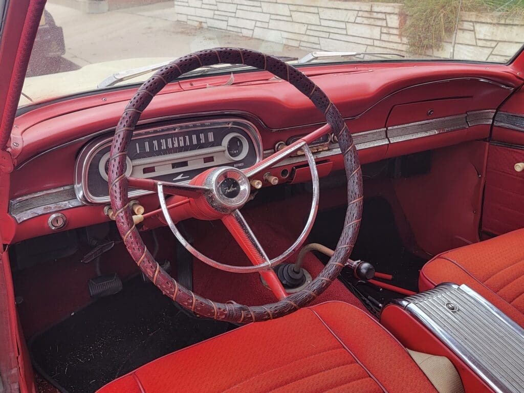 Vintage car interior with red upholstery and classic steering wheel.