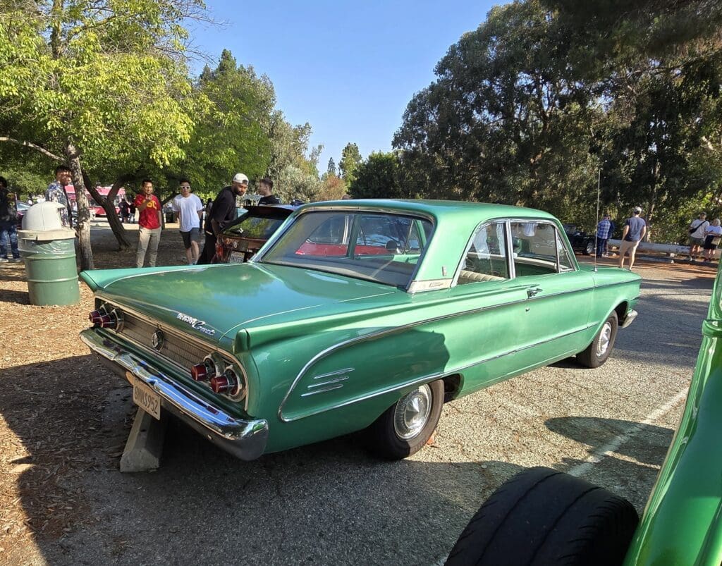 A green classic car displayed outdoors with people in the background.