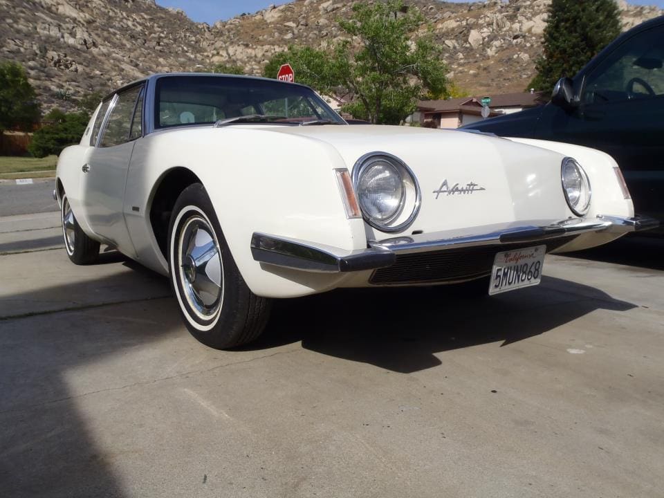 Classic white sports car parked outdoors with mountainous background.
