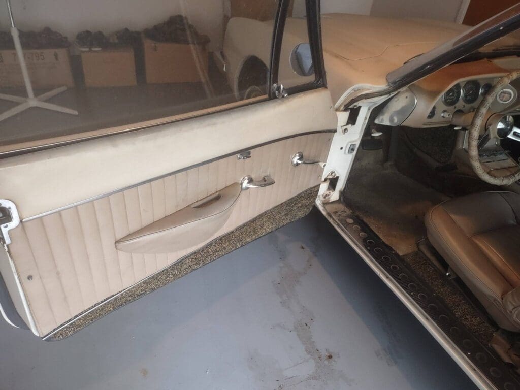 Open vintage car door showing interior panel and handle.