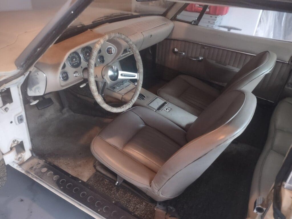 Classic car interior with brown leather seats and vintage steering wheel.