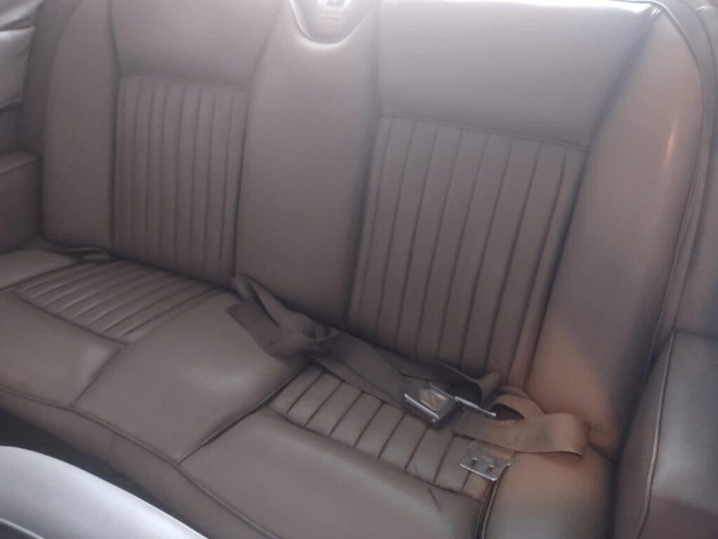 Rear seat of a car with brown leather upholstery and seat belts.