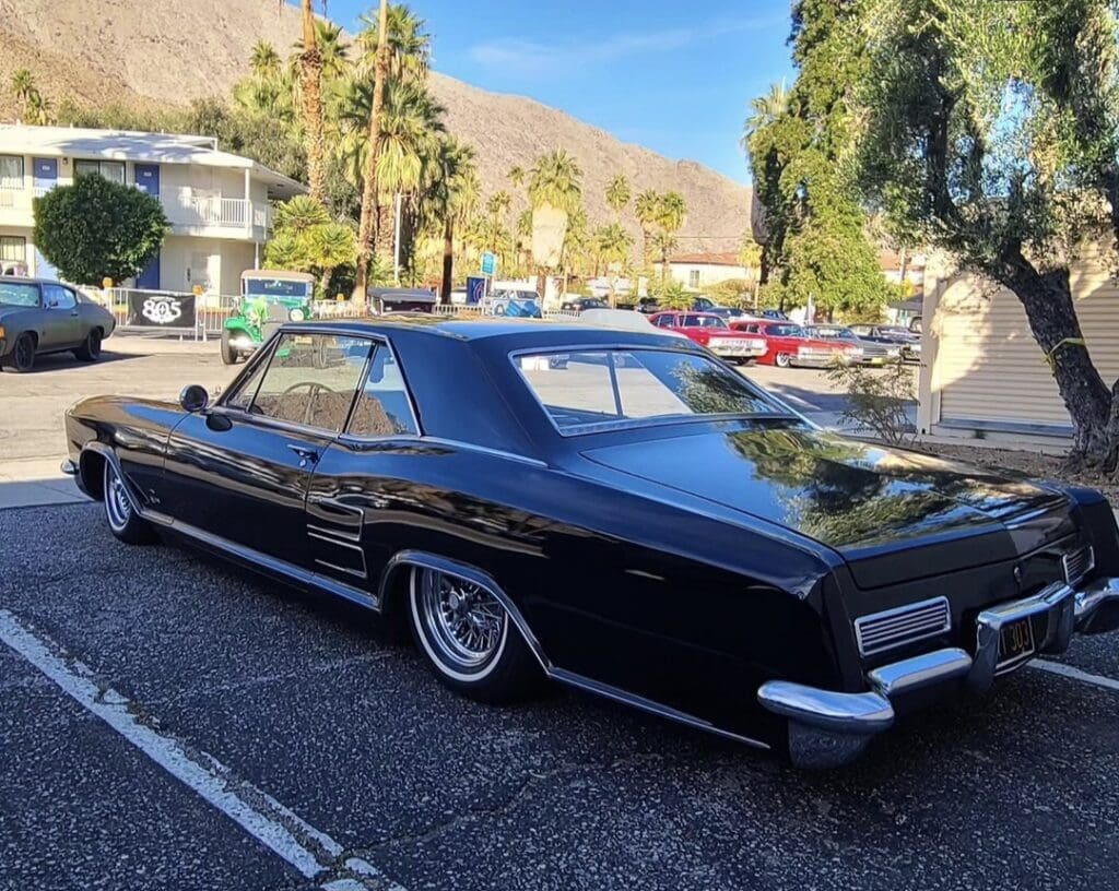 Classic black vintage car parked outdoors with palm trees and mountains in the background.
