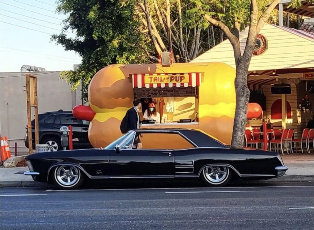 Car parked in front of a giant inflatable hot dog stand.