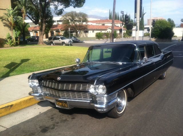 A classic black vintage car parked on a sunny suburban street.
