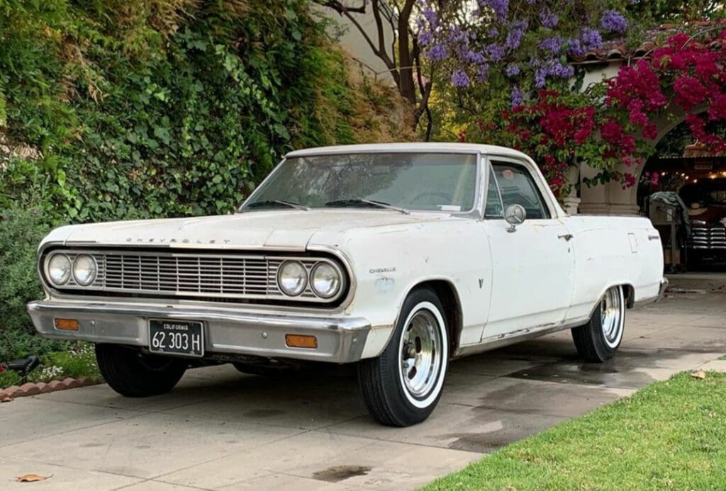 Classic white Chevrolet El Camino parked on a driveway surrounded by greenery.