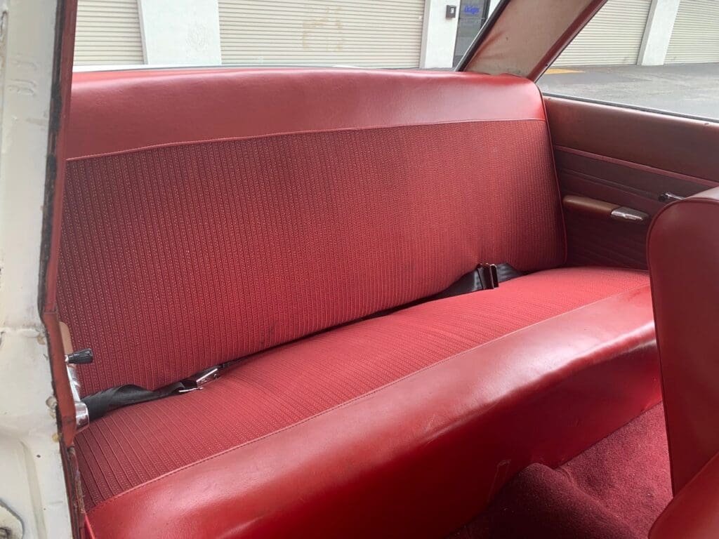 Red vintage car backseat with textured upholstery and seatbelts.